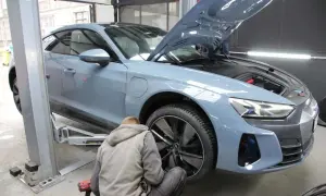 Mechanik przykręca koło niebieskiego samochodu na podnośniku, maska jest otwarta.